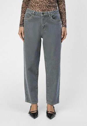 Jeans de mezclilla gris con corte recto, cinco bolsillos y un ligero desgastado. Combinados con tacones de charol negros y punta afilada.