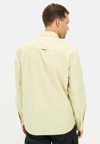 Jasnożółta koszula z długim rękawem, z karczkiem na plecach, mankietami zapinanymi na guziki i minimalnym detalem logo przy dekolcie. Gładka tekstura materiału.