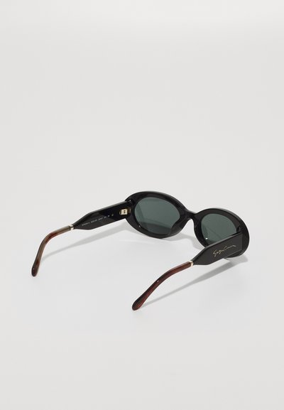 Schwarze Sonnenbrille mit runden Gläsern, grün getöntem Glas und glänzender Oberfläche. Die Bügel haben einen braunen Farbverlauf mit goldenen Markenakzenten.