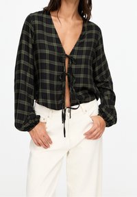 Blusa a costine cropped a quadri neri e verdi con maniche lunghe, scollatura a V e chiusura con cordoncino sul davanti; tessuto testurizzato con polsini arricciati.