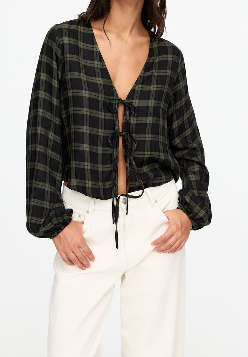 Blusa a costine cropped a quadri neri e verdi con maniche lunghe, scollatura a V e chiusura con cordoncino sul davanti; tessuto testurizzato con polsini arricciati.
