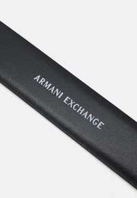 Svart skinnlommebok med preget "ARMANI EXCHANGE"-tekst i sølv. Glatt tekstur, rektangulær form, minimalistisk design.