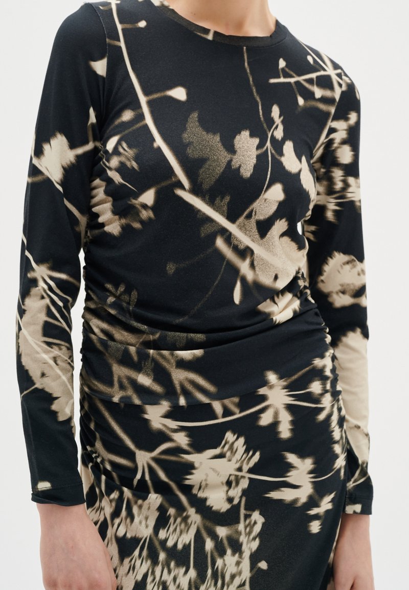 Top de manga larga negro y falda con patrones abstractos florales y de ramas en beige, llevado por una persona frente a un fondo liso.