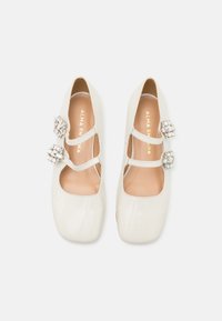 Chaussures Mary Jane couleur crème avec deux brides ornées de bijoux, bouts carrés, et "ALMA EN PENA" imprimé à l'intérieur de chaque chaussure.