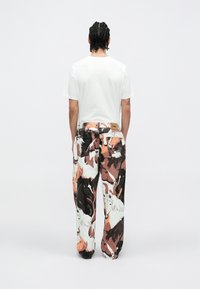 Fehér póló és színes nadrág, amelyek fekete, fehér és narancs lónyomattal készültek. A nadrág hátulján barna címke található.