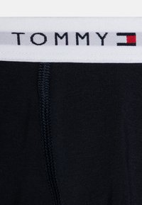 Boxer briefs neri in cotone con un elastico bianco in vita che presenta il logo "TOMMY" e accenti rossi e blu. Texture liscia e cuciture ricamate.