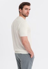 Kortärmad, krämfärgad polo med textur och ribbade ärmslut, kombinerad med ljusgrå byxor med ränder. Enkelt design.