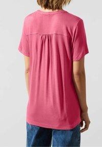 T-shirt rosa a maniche corte con dettaglio di cucitura aderente sul retro. Materiale di cotone morbido con una vestibilità ampia e rilassata. Collo rotondo casual.