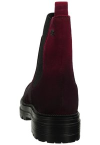 Bota de ante burdeos hasta el tobillo con paneles laterales elásticos negros, puntera redondeada y suela negra gruesa. Presenta un logo en relieve cerca del talón.