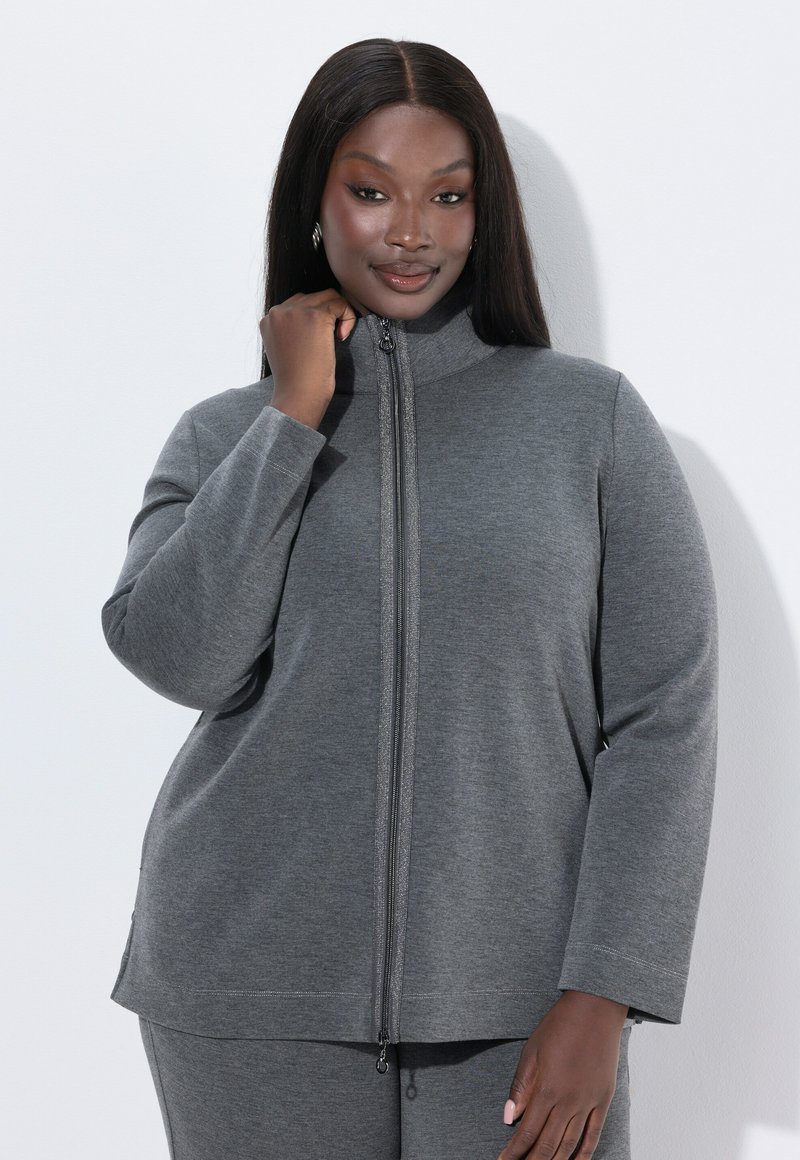 Veste grise zippée avec un col montant, des manches longues et une coupe décontractée. Fabriquée en tissu doux et texturé avec une fermeture éclair à l'avant.