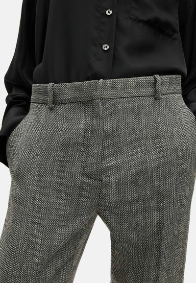Pantaloni tailored grigio houndstooth con design a gamba dritta, tessuto texturizzato, passanti per cintura e tasche laterali, abbinati a una camicia nera.