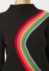 Černý žebrovaný svetr s diagonálním, vícebarevným pruhovaným vzorem v červené, růžové, žluté, zelené a šedé. Vysoký límec.