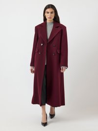 Cappotto bordeaux doppiopetto in lana, con ampi risvolti, due tasche frontali e tessuto testurizzato, abbinato a una maglietta grigia e pantaloni neri.