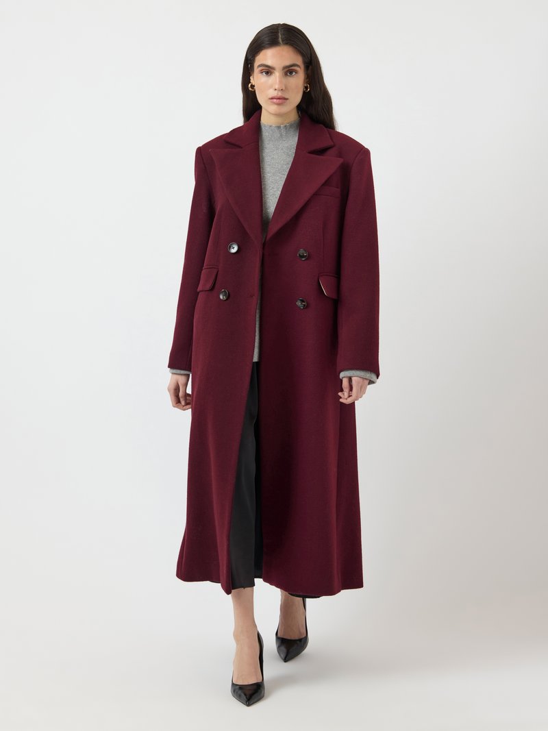 Cappotto bordeaux doppiopetto in lana, con ampi risvolti, due tasche frontali e tessuto testurizzato, abbinato a una maglietta grigia e pantaloni neri.