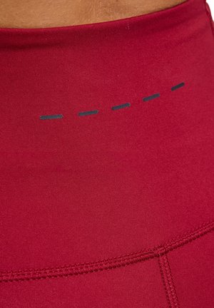 Gros plan sur des leggings de sport rouges avec une taille haute, une ligne réfléchissante horizontale en pointillés et des coutures détaillées.