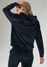 Navy velours hoodie met een ontspannen pasvorm, voorzien van een trekkoord capuchon en geribde manchetten. Soepele textuur, in stijl met bijpassende broeken.