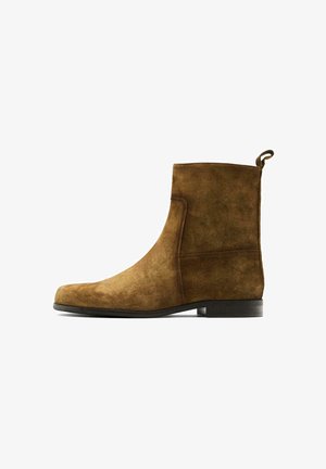 Stivaletto in suede marrone con punta arrotondata, dettagli di cucitura laterale e una piccola linguetta sul retro. Suola piatta e nera.