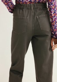 Pantaloni verde scuro con elastico in vita, due tasche posteriori, design a gamba affusolata e texture morbida, abbinati a una maglietta con stampa floreale.