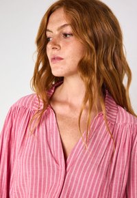 Blusa rosa a righe con scollatura a v profonda e chiusura senza bottoni, caratterizzata da una vestibilità morbida e un tessuto leggero e soffice.