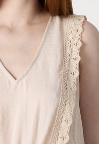Beige ilmahalu blouse V-kaelusega ja pitsiga kaeluse ääres. Pehme kangas, millel on veidi kortsus tekstuur ja lõdva lõikega.