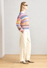 Mehrfarbiger gestrickter Pullover mit horizontalen Streifen, kombiniert mit weiten beigen Hosen und spitzen metallic-farbenen Absätzen. Grüne Sonnenbrille wird getragen.