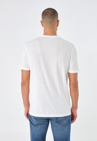 White cotton t-shirt with short sleeves, crew neckline, and a plain texture, paired with blue denim jeans featuring back pockets.