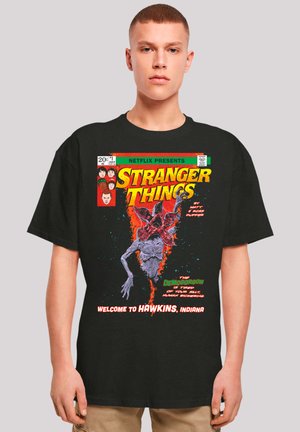 Black cotton t-shirt featuring "Stranger Things" graphic. The design includes a Demogorgon and text in vibrant yellow and white on a colorful background.