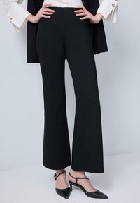 Svarta vida byxor i ett mjukt, stretchigt material. Har hög midja och en ren fåll. Kombineras med spetsiga svarta klackar.