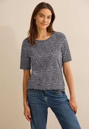 Haut bleu marine à manches courtes avec un motif géométrique blanc, col rond et coupe décontractée, associé à un jean bleu clair.