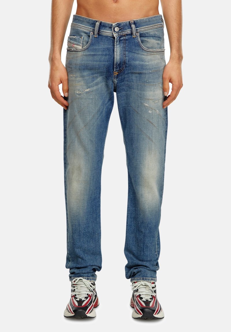 Vaqueros de denim azul con un acabado desgastado, cinco bolsillos y un leve deterioro. Talle estándar y diseño de pierna recta.