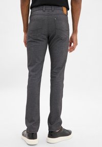 Szare spodnie z teksturowanym wzorem, pięcioma kieszeniami i brązową skórzaną łatą z tyłu. Noszone z czarnymi trampkami.