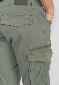 Groene cargobroek met meerdere zakken, een voorzak met rits en een gladde, gestructureerde stof. Voorzien van een leren label op de tailleband.