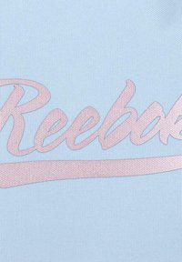 Primer plano de una tela texturizada azul claro con texto en cursiva rosa en relieve que dice "Reebok" a lo largo de la superficie.