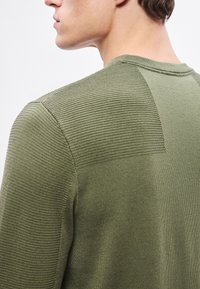 Olíva zöld pulóver texturált bordás mintával a vállakon. Kerek nyakkivágás, testhez simuló szabás, sima hátoldal, könnyű anyag.