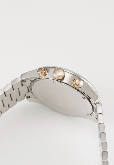 Montre en acier inoxydable argenté avec un bracelet texturé, trois poussoirs dorés, et un boîtier poli. L'arrière est lisse avec un logo imprimé.
