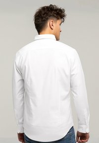 Biała koszula z długim rękawem, z kołnierzykiem zapinanym na guziki, w dopasowanym kroju i prostym wykończeniu. Wykonana z gładkiej bawełny z mankietami zapinanymi na guziki.