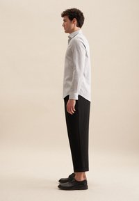 Camicia bianca a maniche lunghe con un motivo sottile, abbinata a pantaloni neri e scarpe nere. Presenta un colletto a rovescio e chiusura con bottoni.