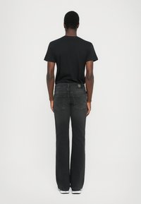 Črne jeans hlače s ravnim krojem, petimi žepi in diskretno oznako na hrbtni strani. Gladka tekstura in minimalni detajli.
