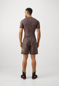 Camiseta atlética castanha de mangas curtas com um padrão texturizado, acompanhada de calções a condizer com um cós elástico e um detalhe de logotipo.