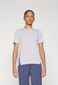 Camisola atlética curta de manga, na cor lilás claro, com decote redondo, acabamentos em malha nas laterais e um pequeno logotipo branco no peito.