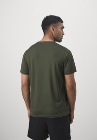 Camiseta corta de manga corta en verde oscuro con una textura acanalada, escote redondo y un ajuste relajado, mostrada desde la parte de atrás.