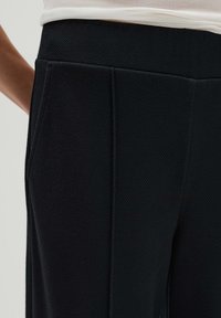 Pantalons noirs en tissu texturé avec une taille haute, des plis prononcés et des poches latérales pour plus de fonctionnalité.