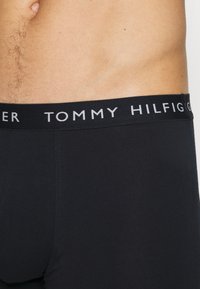 Schwarze Baumwoll-Boxershorts mit breitem elastischem Bund, auf dem der "TOMMY HILFIGER"-Schriftzug in weißer Schrift zu sehen ist. Glatte Textur und enganliegendes Design.