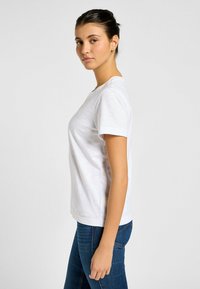 T-shirt bianco a maniche corte con collo rotondo, realizzato in tessuto leggero, abbinato a jeans blu aderenti. Texture liscia, design semplice.