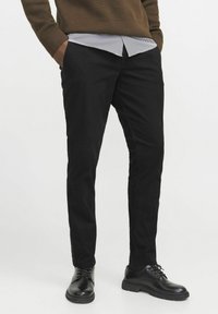 Black slim-fit pants made of cotton blend, featuring a smooth texture. Paired with a striped shirt and black shoes.