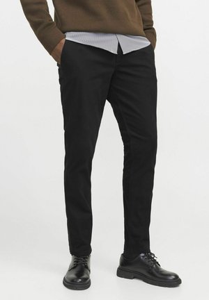 Schwarze Slim-Fit-Hosen aus Baumwollmischung mit einer glatten Textur. Kombiniert mit einem gestreiften Hemd und schwarzen Schuhen.