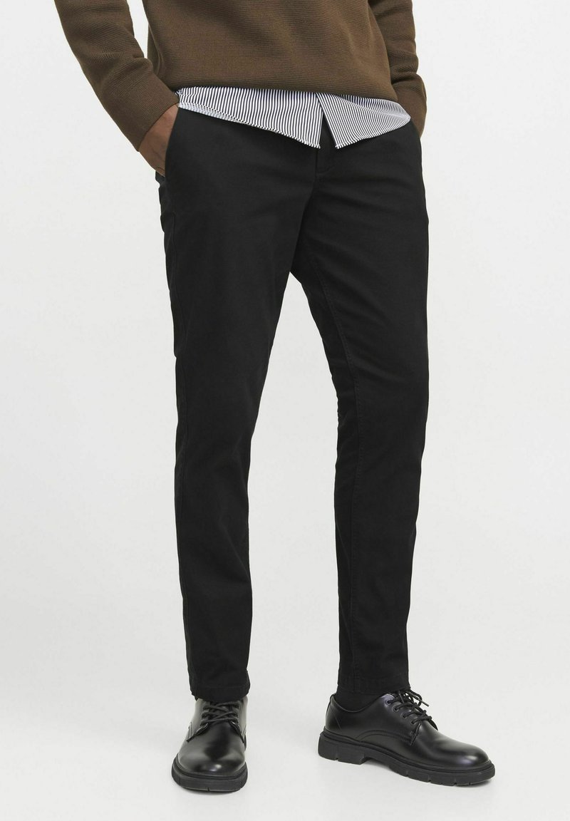 Black slim-fit pants made of cotton blend, featuring a smooth texture. Paired with a striped shirt and black shoes.