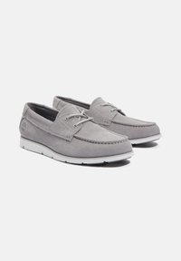 Scarpe da barca in suede grigio con suole in gomma bianca. Le caratteristiche includono lacci, cuciture a contrasto e un logo impresso sul lato.