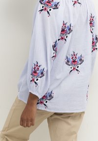 Světle modrá proužkovaná halenka s květinovou výšivkou v červené, růžové a modré. Volný střih, nařasené rukávy a kulatý výstřih.