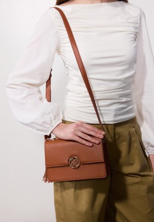 Brown leather crossbody bag with a gold circular accent, rectangular shape, flat design, and long adjustable strap.